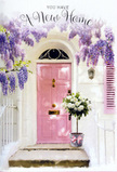 In this image, a Chislehurst entrance is turned into an intimate celebration of arrival, framed entirely by flowers and soft colour. The focal point is a front door painted in a delicate shade of pink, the kind of calming blush that seems to absorb and soften the daylight drifting in from a quiet, tree-lined street. The surrounding wall is whitewashed and subtly textured, catching little streaks of light and shadow that add depth without cluttering the view. A single shutter, painted to match the door, creates a sense of balance and continuity across the façade. Arching above and trailing down around the door is a generous growth of wisteria, its long clusters of flowers hanging in cascades of lavender, lilac, and pale purple. The blossoms gather densely at the top and then thin out as they fall, giving a sense of graceful movement, while interlaced green leaves lend the structure of a living garland. At the foot of this floral frame sits a simple grey metal bucket, the kind often used by experienced florists. From it spills a luxurious bouquet of white and cream roses, tightly packed yet individually visible, each petal catching the light with soft, creamy highlights. Small touches of fresh green foliage thread between the blooms, echoing the wisteria's leaves and tying the whole composition together. Wrapped around the base of the bucket is a pink ribbon, tied in a tender bow whose hue mirrors the door above. The scene feels perfectly poised for a housewarming in Chislehurst, like a thoughtful delivery from a local florist who understands how a single arrangement on the step can turn an unfamiliar doorway into a place that already feels loved and lived in.